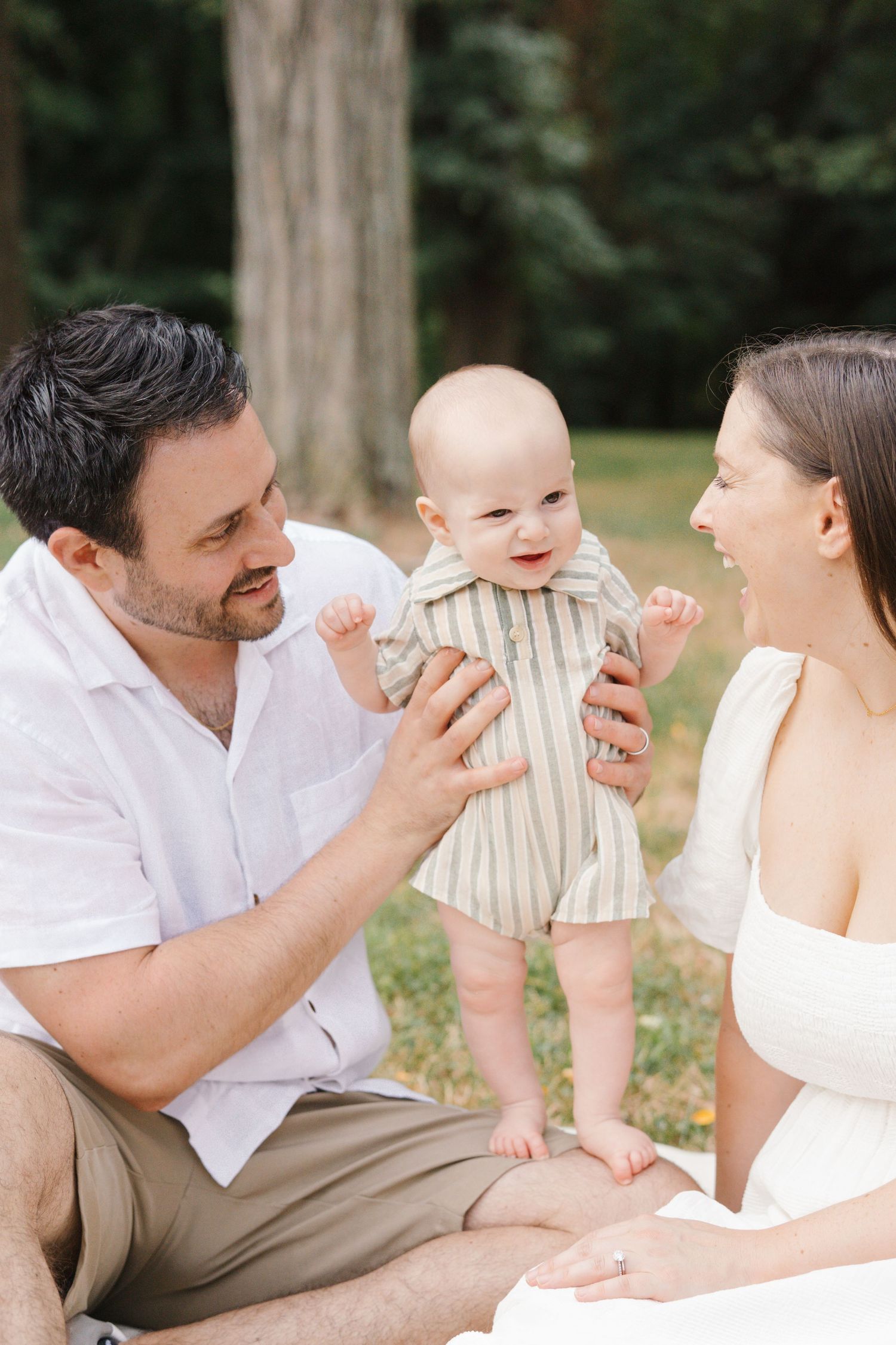 A happy family moment captured outdoors with their baby in a striped outfit.