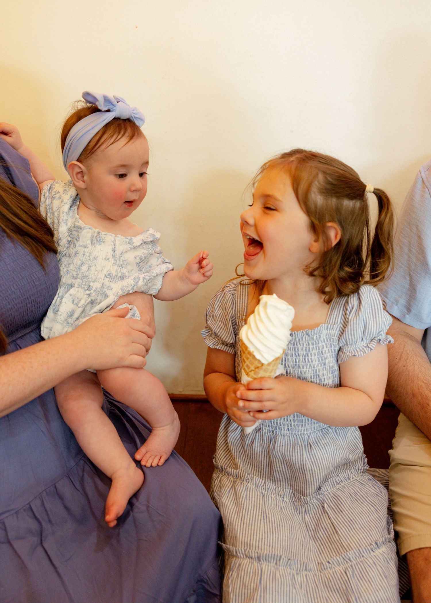 Two small children in blue and white outfits enjoy ice cream cones while sitting together.