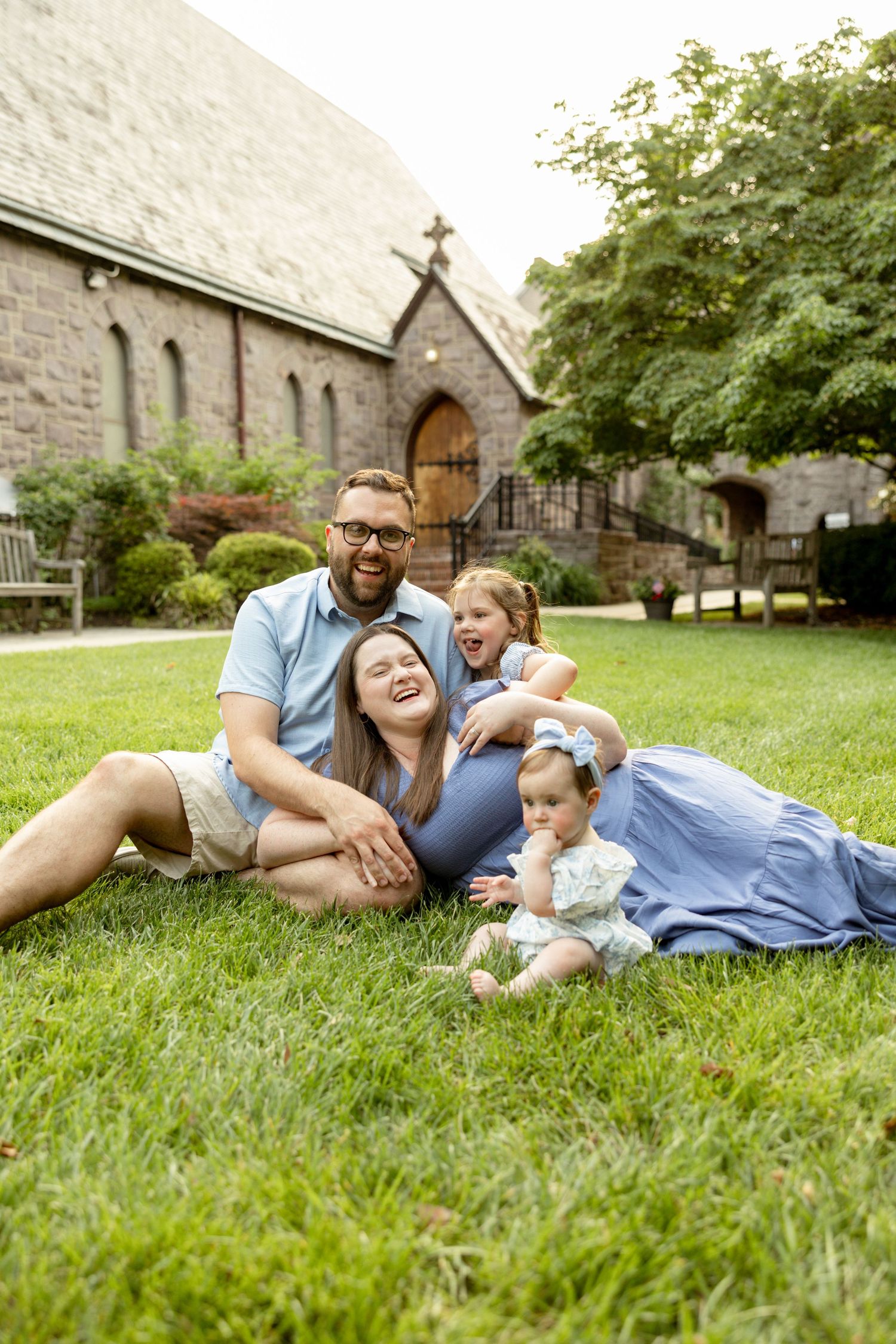 Family enjoying quality time together while laying on green grass outside a stone church building on a sunny day.