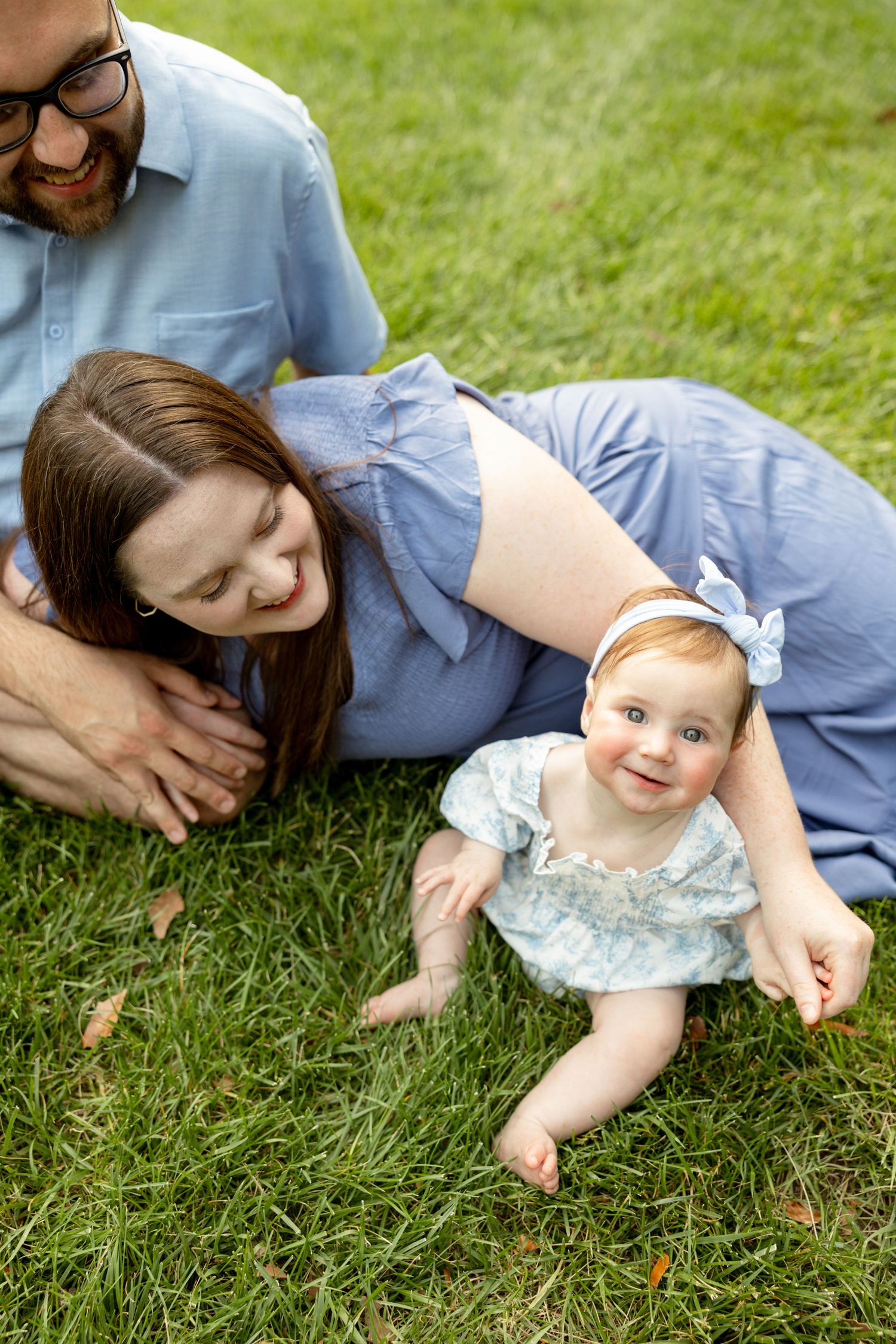A family laying together on green grass outdoors, enjoying a warm summer day in casual attire.