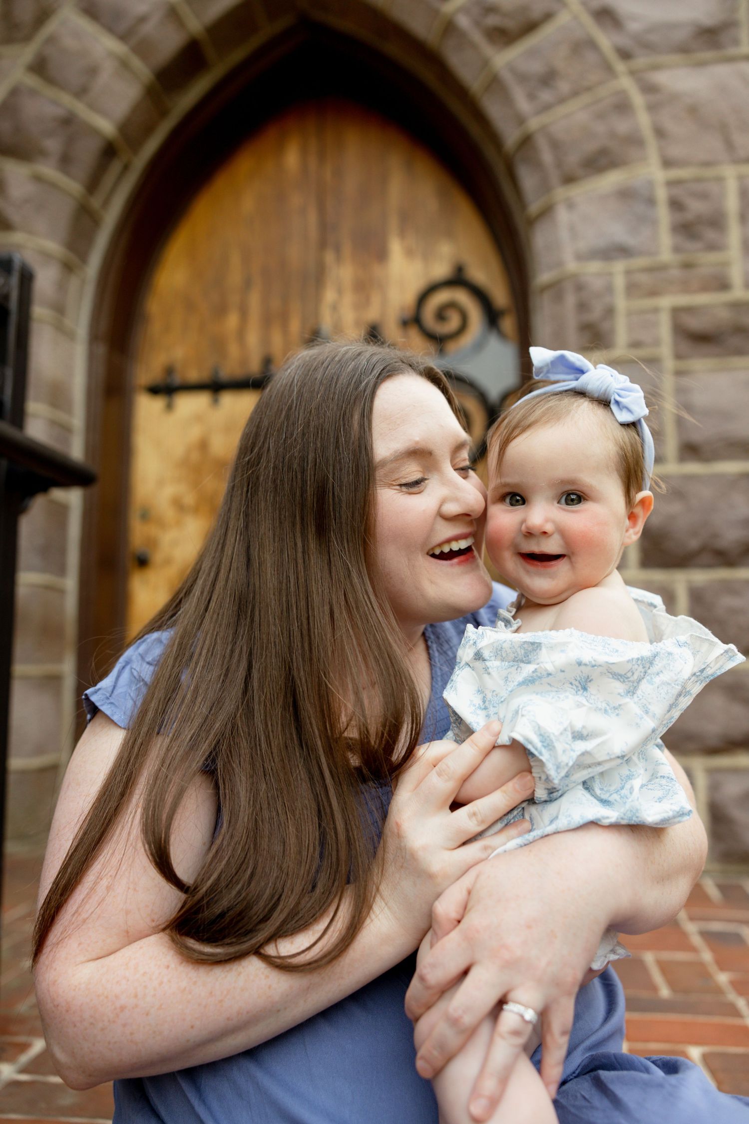 A joyful moment shared between parent and baby in front of a gothic stone archway with wooden door.