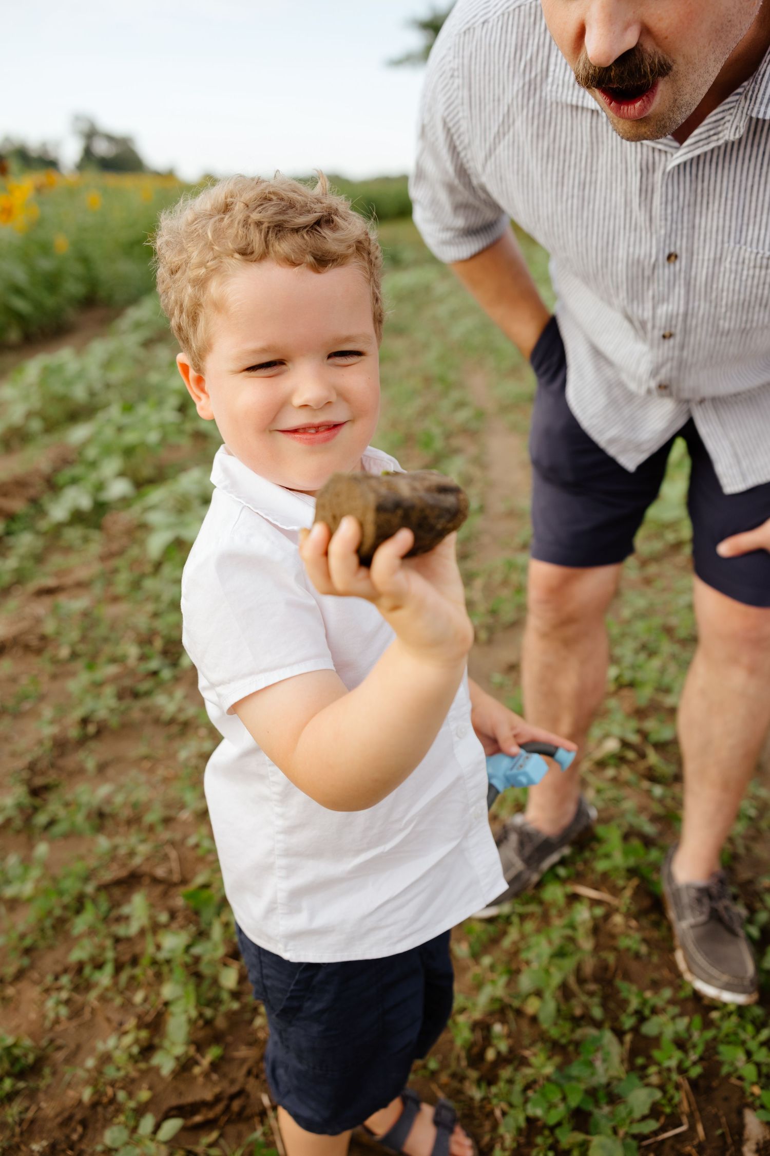 A young child excitedly eating fresh berries while standing in a field with plants and rows of greenery.