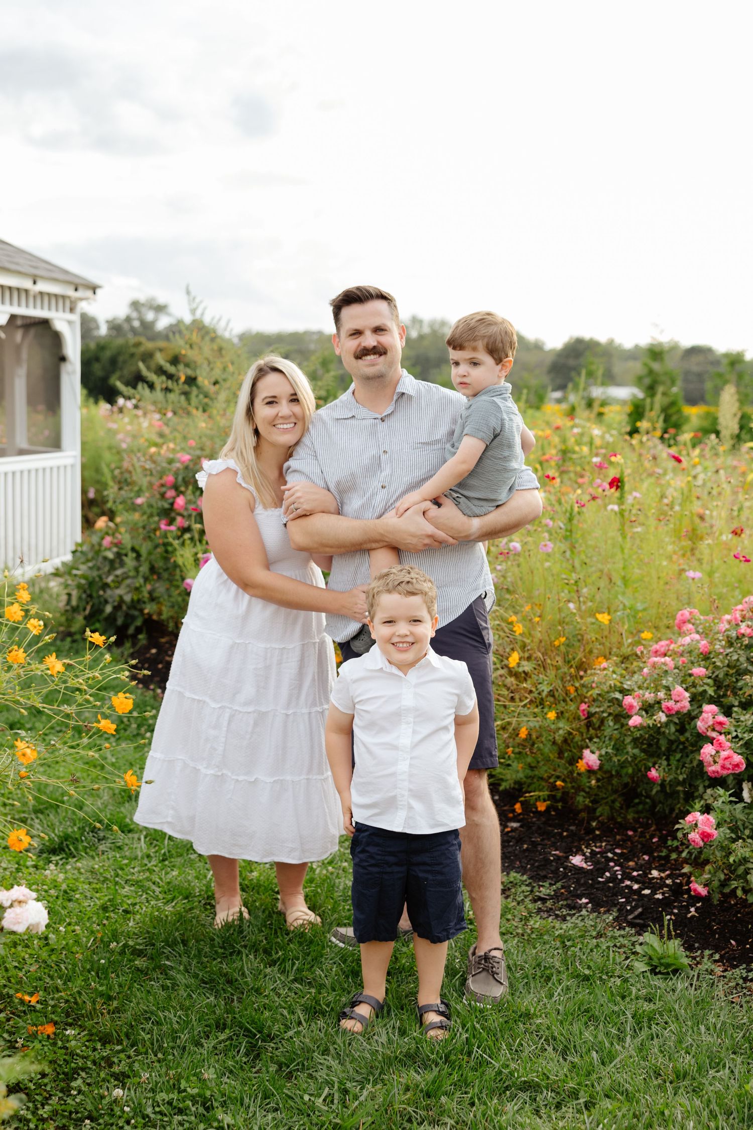 Family enjoying a summer evening in a garden filled with colorful wildflowers and blooming shrubs by a white fence.