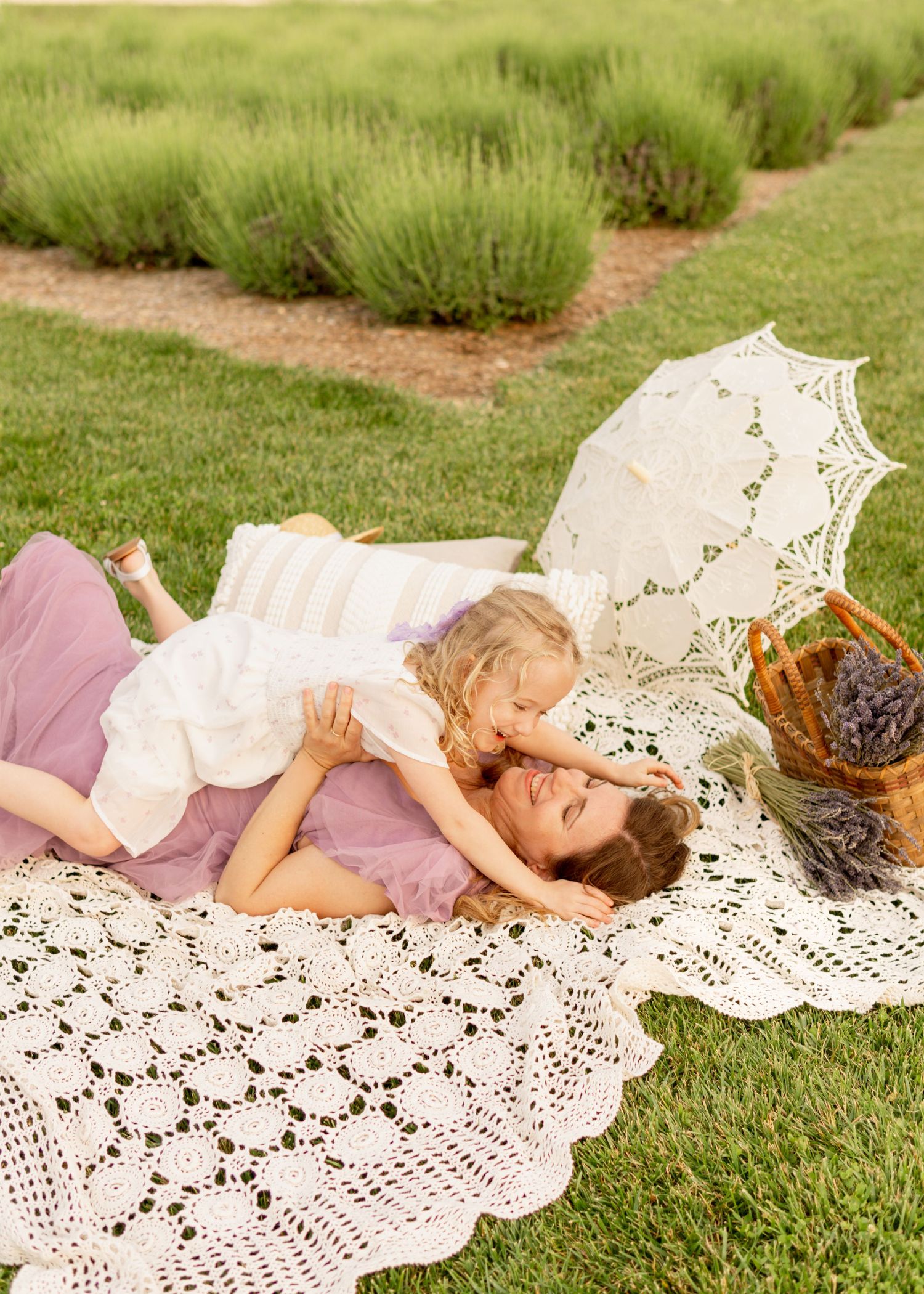 A picnic moment on a white lace blanket in a garden with a vintage parasol and wicker basket nearby.