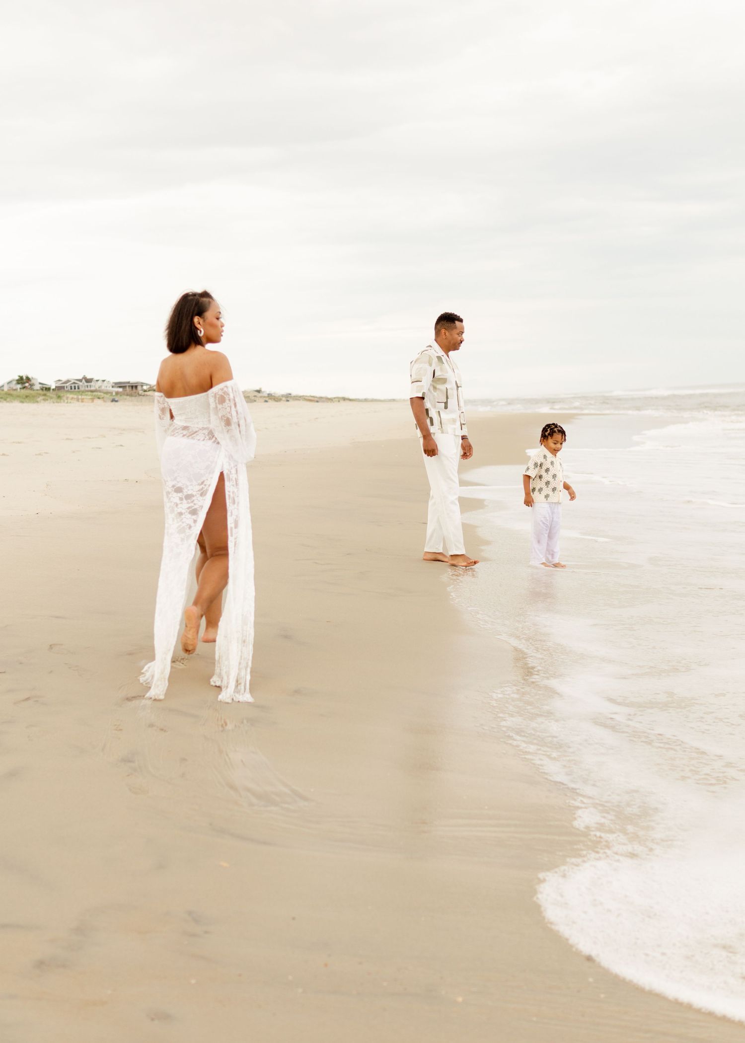 A group in white clothing walks along a misty beach shoreline at sunset creating a serene coastal scene.