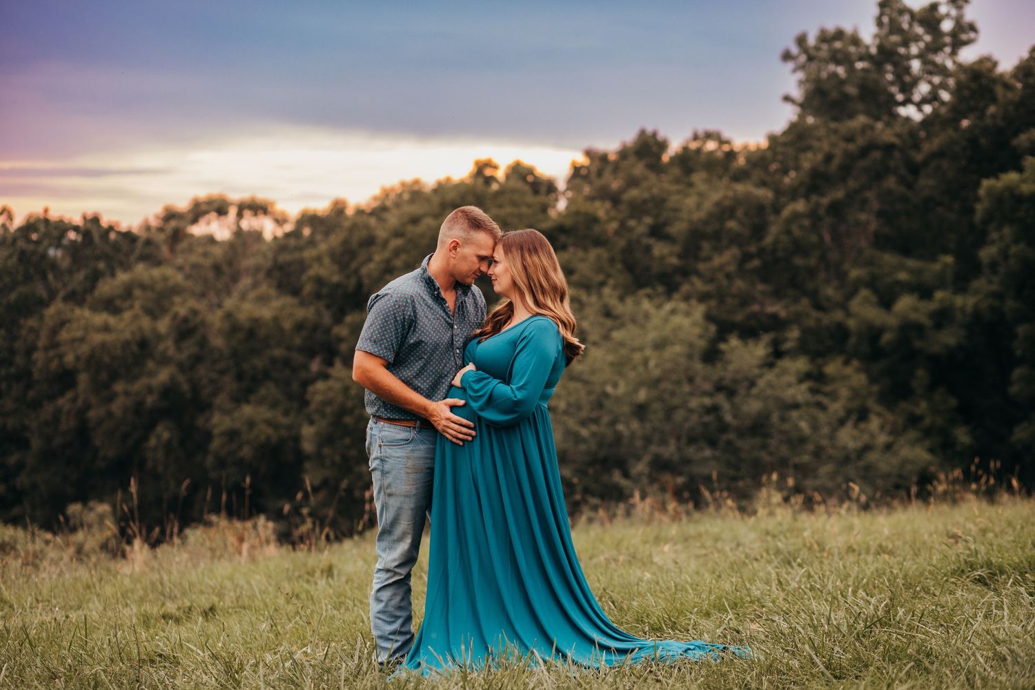 Couple embraces in a field at sunset, with her wearing a flowing teal dress.