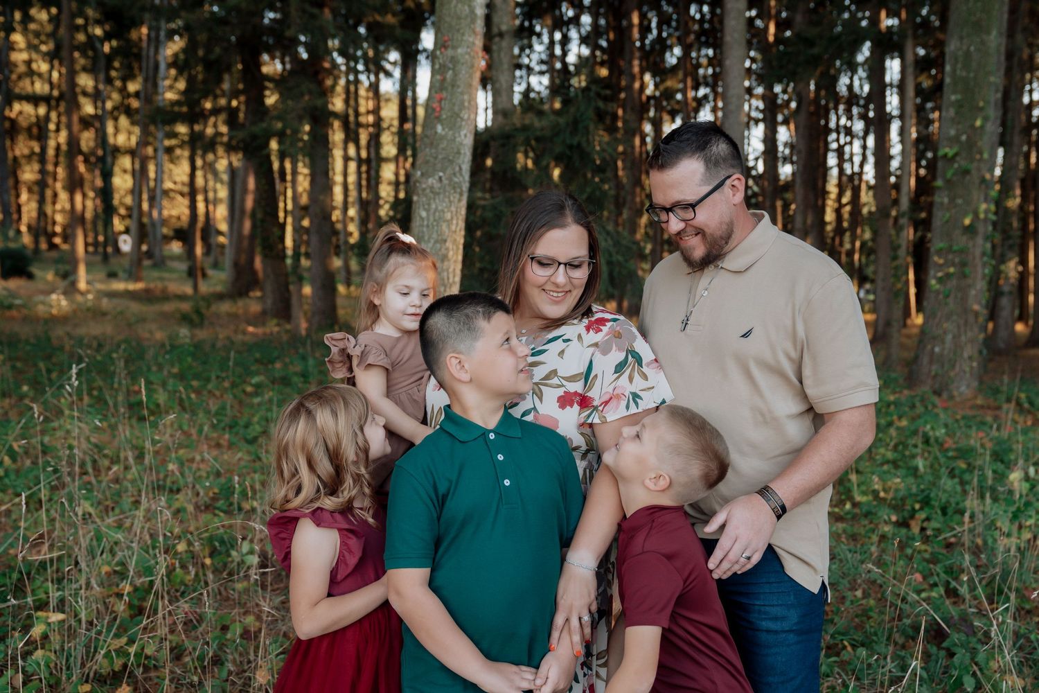 Happy family of six shares a joyful embrace among tall pine trees during an outdoor fall photo session.