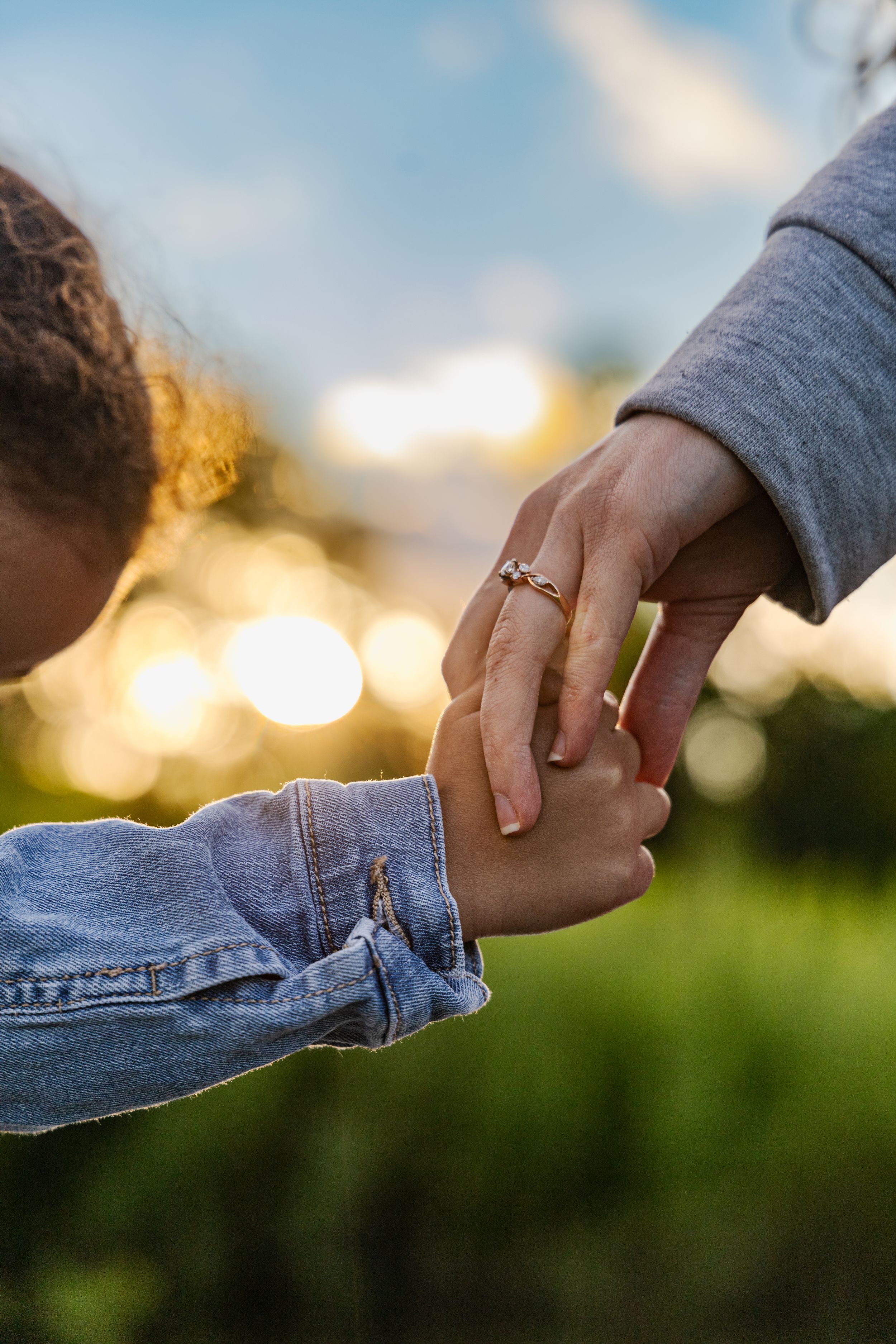 A women holding the hand of her little one outside walking in the grass
