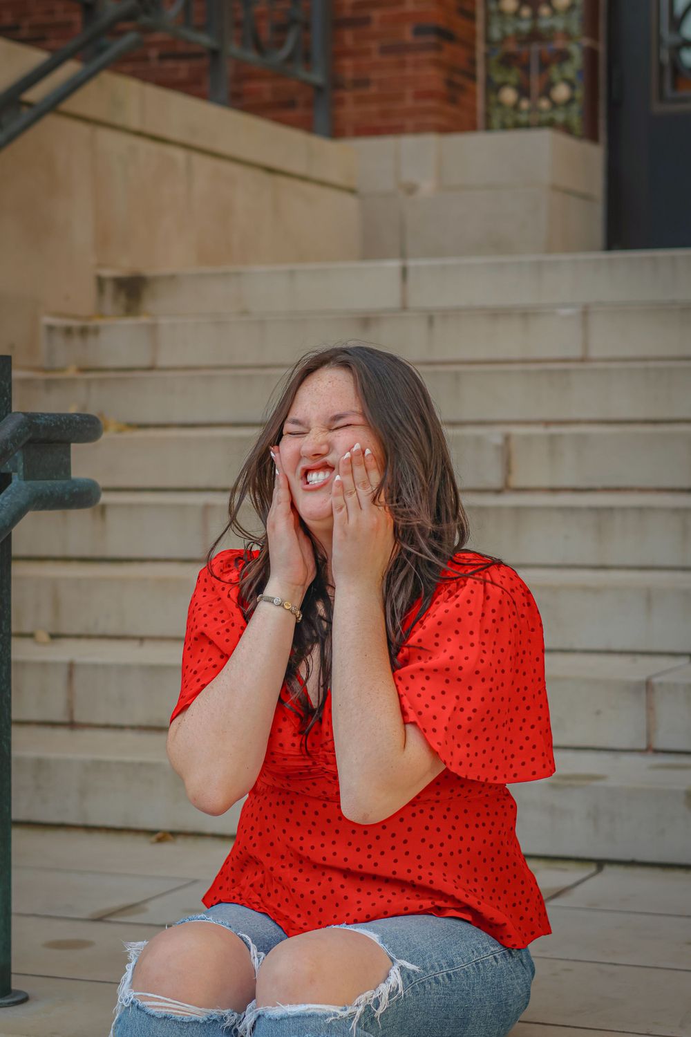 Person in red polka dot top laughing while sitting on concrete steps.