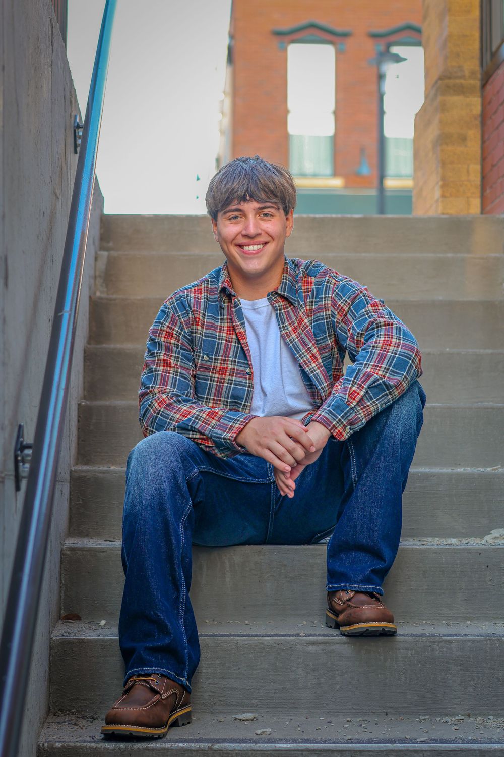 Person in plaid shirt and jeans sitting on concrete steps in urban setting.
