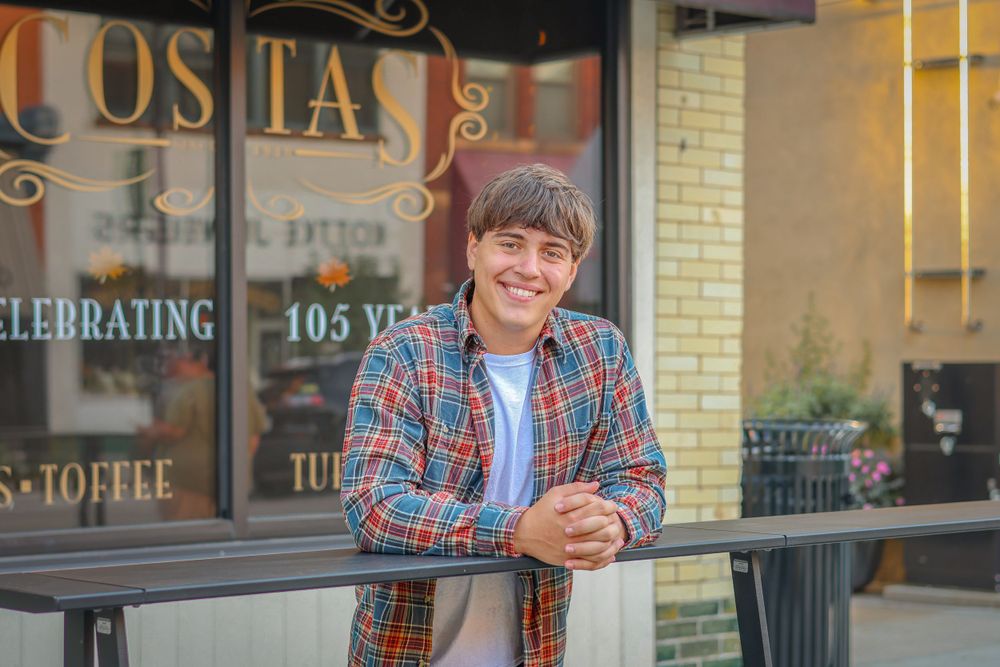 Person in casual attire leaning on railing outside historic Cosita storefront.