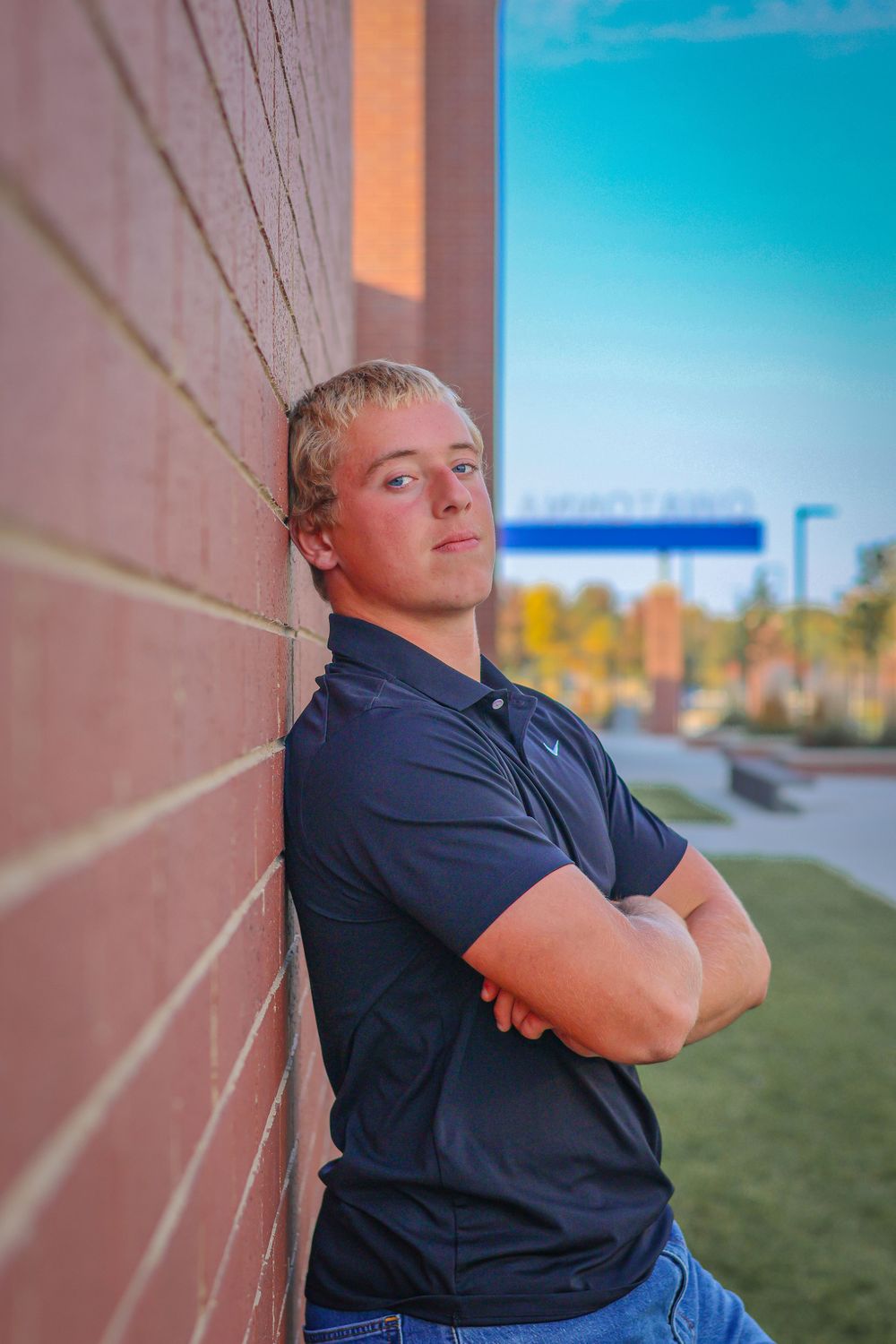 Portrait against brick wall with autumn colors and blue sky in background.
