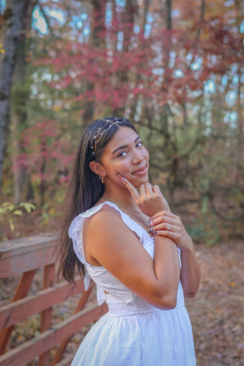 A woman in white dress poses thoughtfully against autumn forest backdrop.