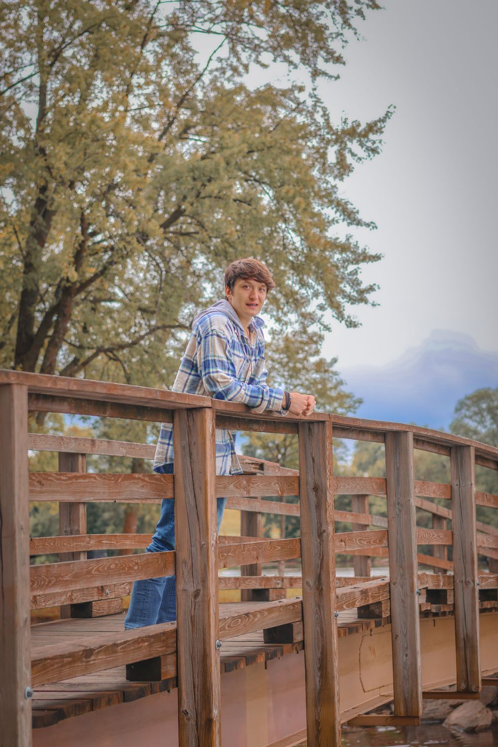 Casual autumn portrait on wooden bridge deck with trees and mountains in background.
