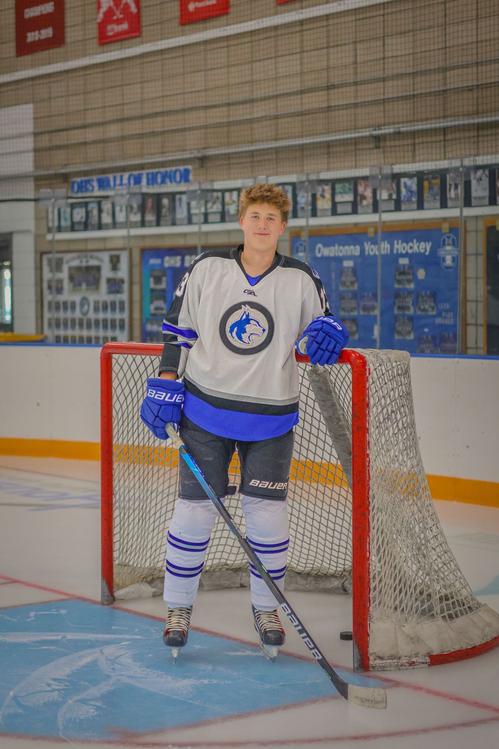 Hockey player stands in front of goal net wearing white jersey with blue trim.