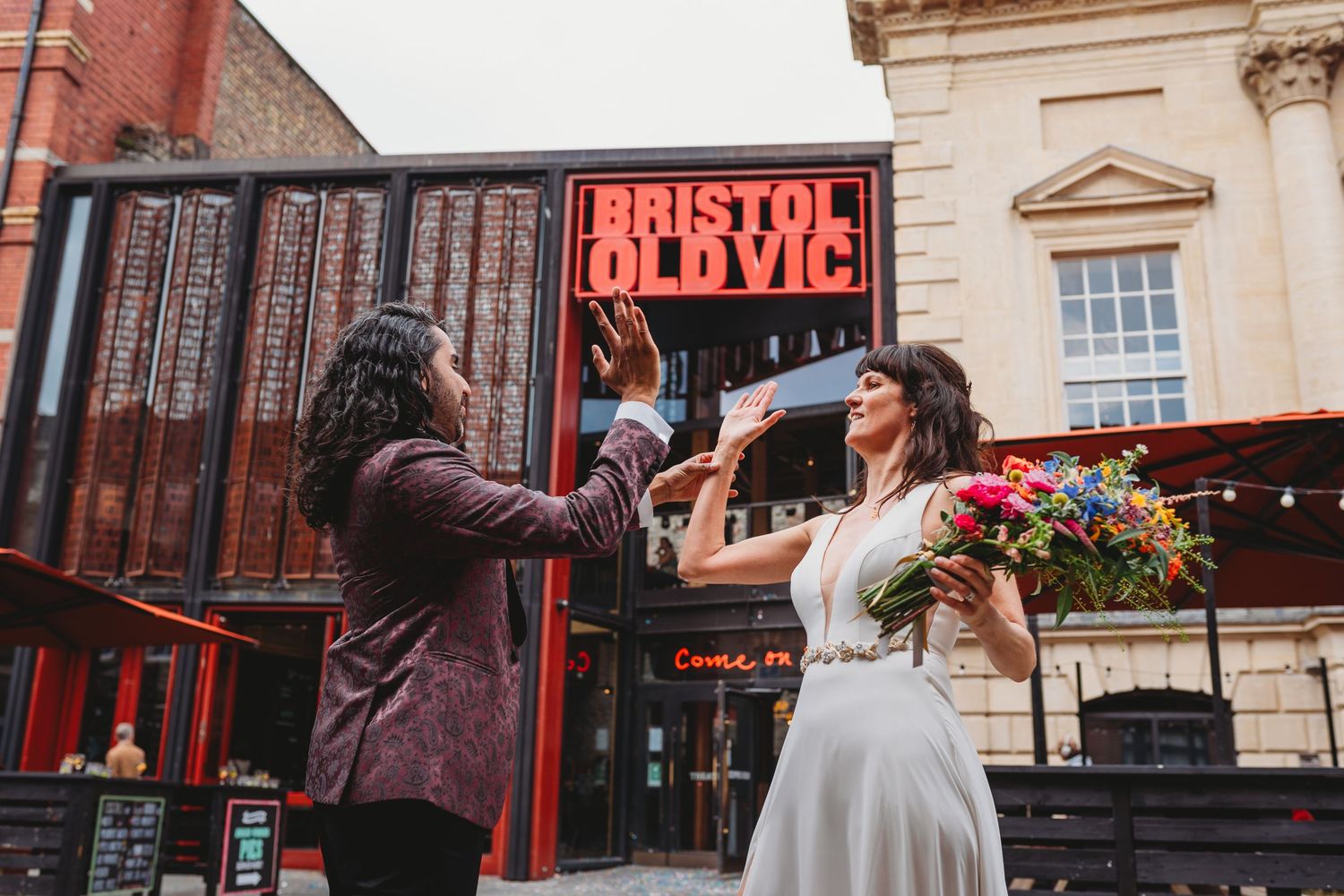Wedding scene outside Bristol Old Vic theater with colorful bouquet.