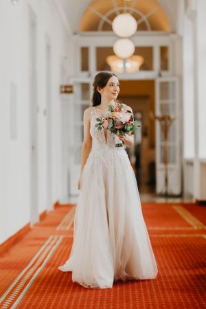 Elegant white wedding gown in grand hallway with arched details and red carpet.