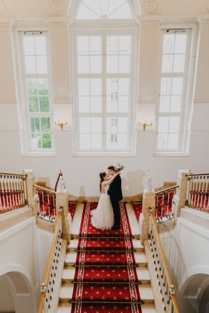 Grand staircase with red carpet runner and white columns in elegant wedding venue.