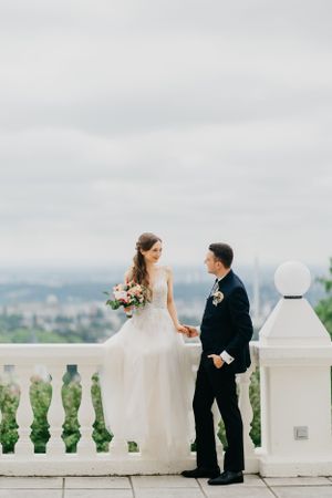 Elegant wedding couple on white balcony overlooking scenic landscape.
