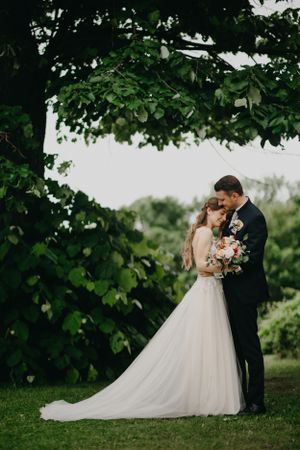 Romantic wedding portrait under green tree canopy in garden setting.