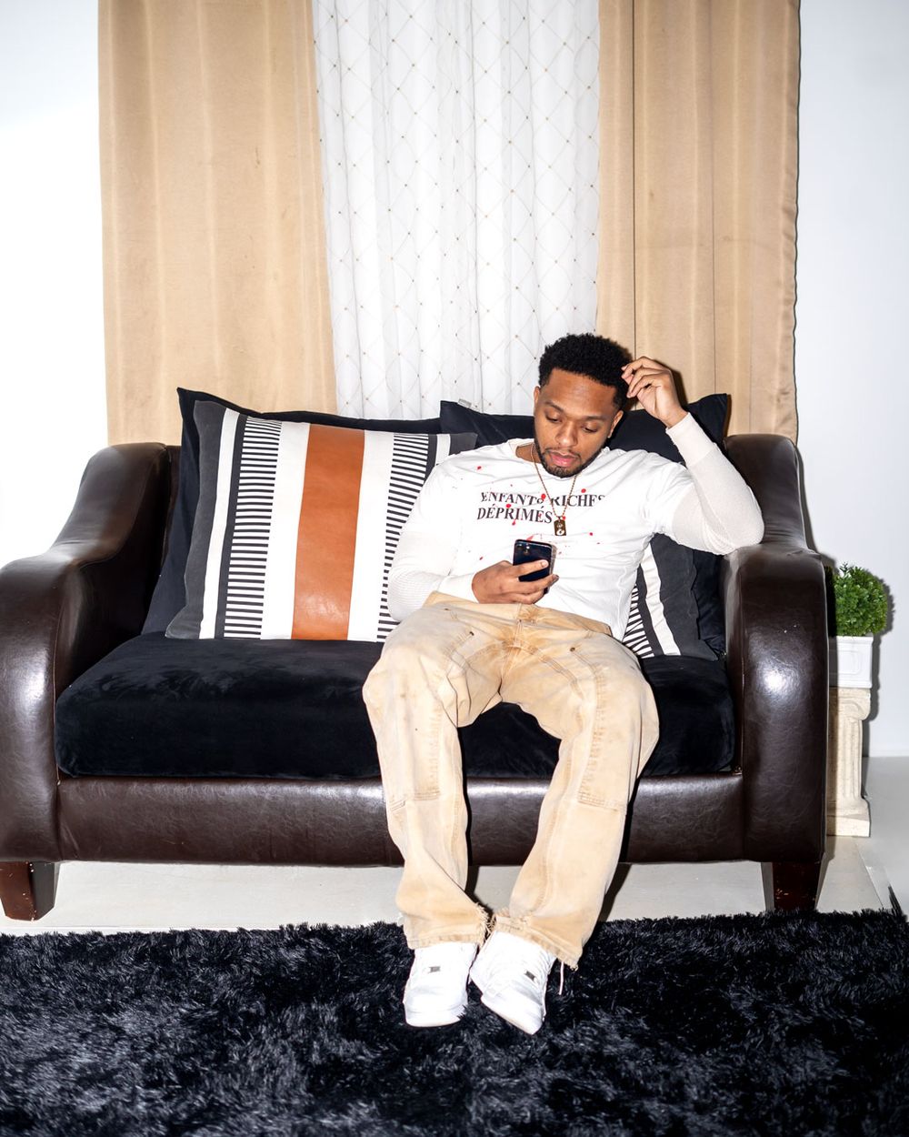 Person relaxing on a leather couch wearing a white sweatshirt and beige pants with white sneakers.