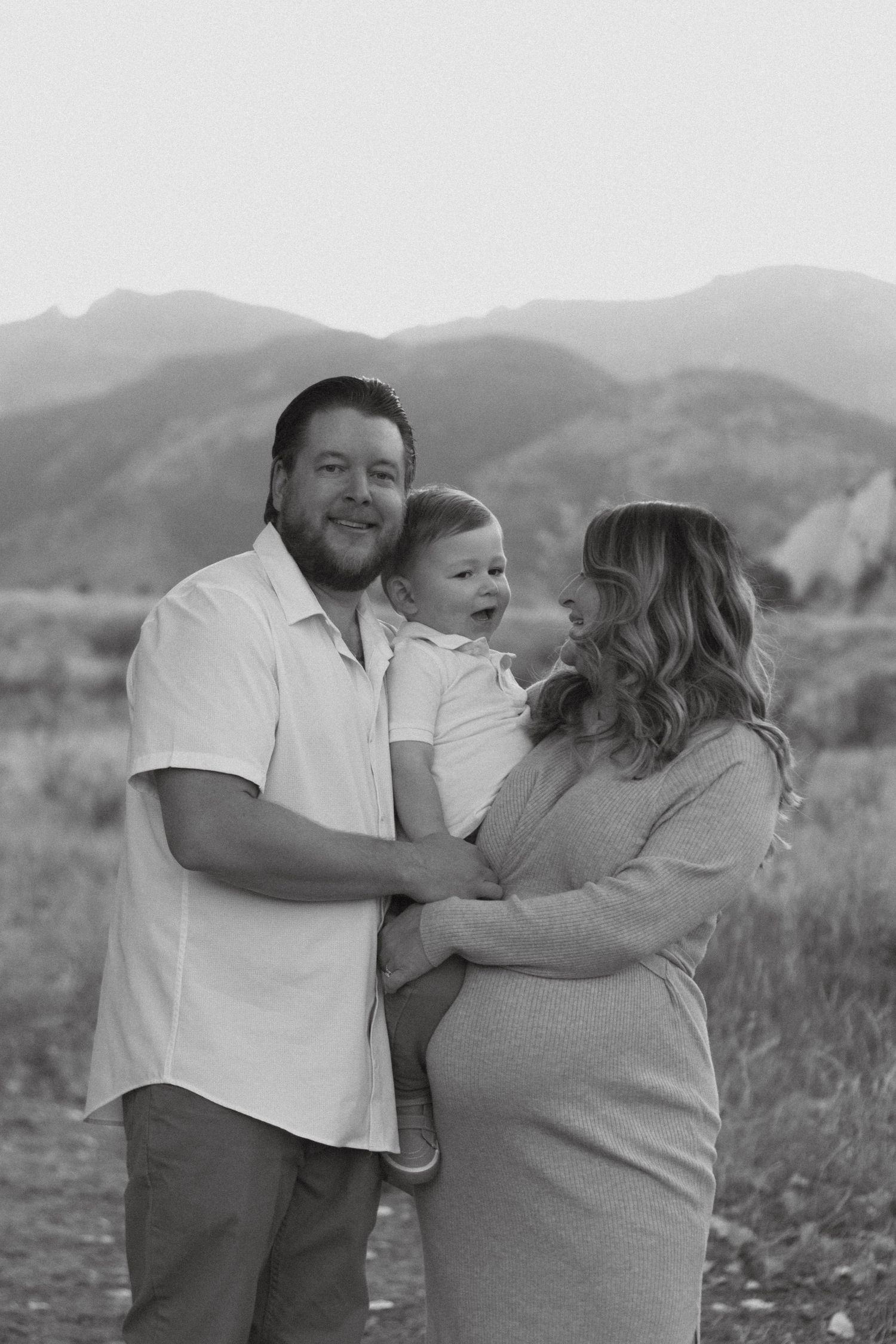 A family shares a moment together outdoors with mountains in the background in black and white. Family photoshoot Colorado, Red rocks