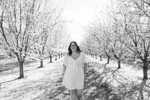 Woman in white dress walking through blossoming orchard in black and white photo.