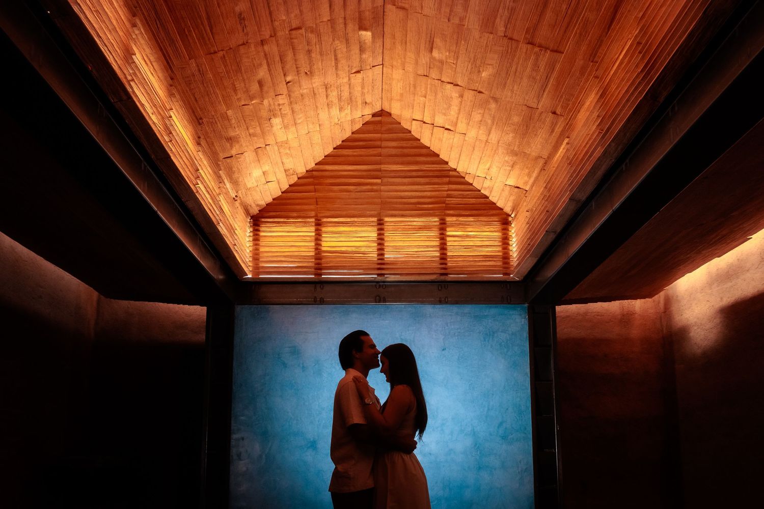 Romantic silhouettes under wooden ceiling with dramatic lighting and blue walls.