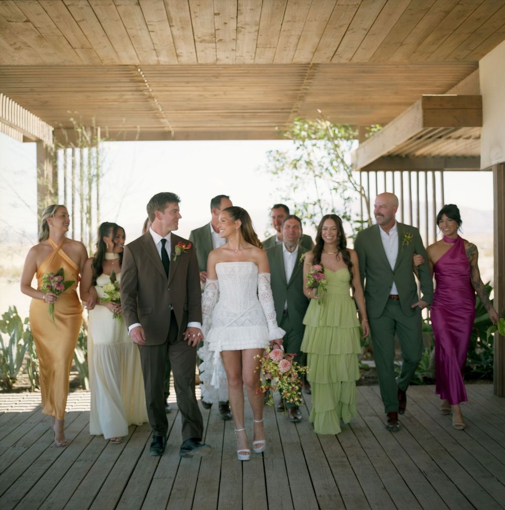 Wedding party walking together outdoors, bride in white mini dress with bridesmaids and groomsmen.