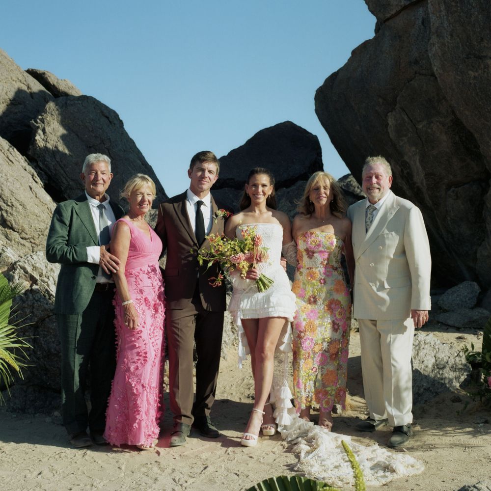 Wedding party of six poses together among large rocks in sunny outdoor desert setting.