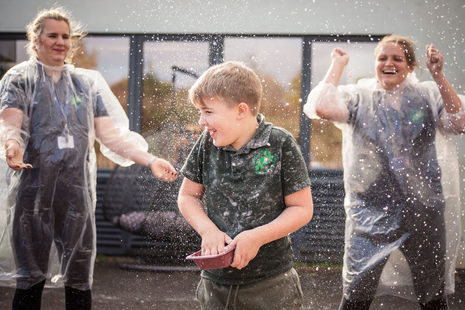 Child having coloured flour thrown at them in a Holi type celebration by teachers in overalls