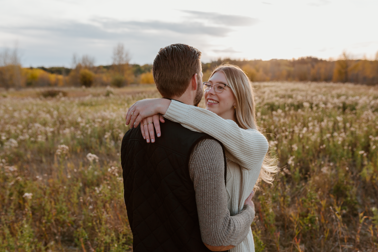 Couple sitting down near a river looking at each other and smiling.