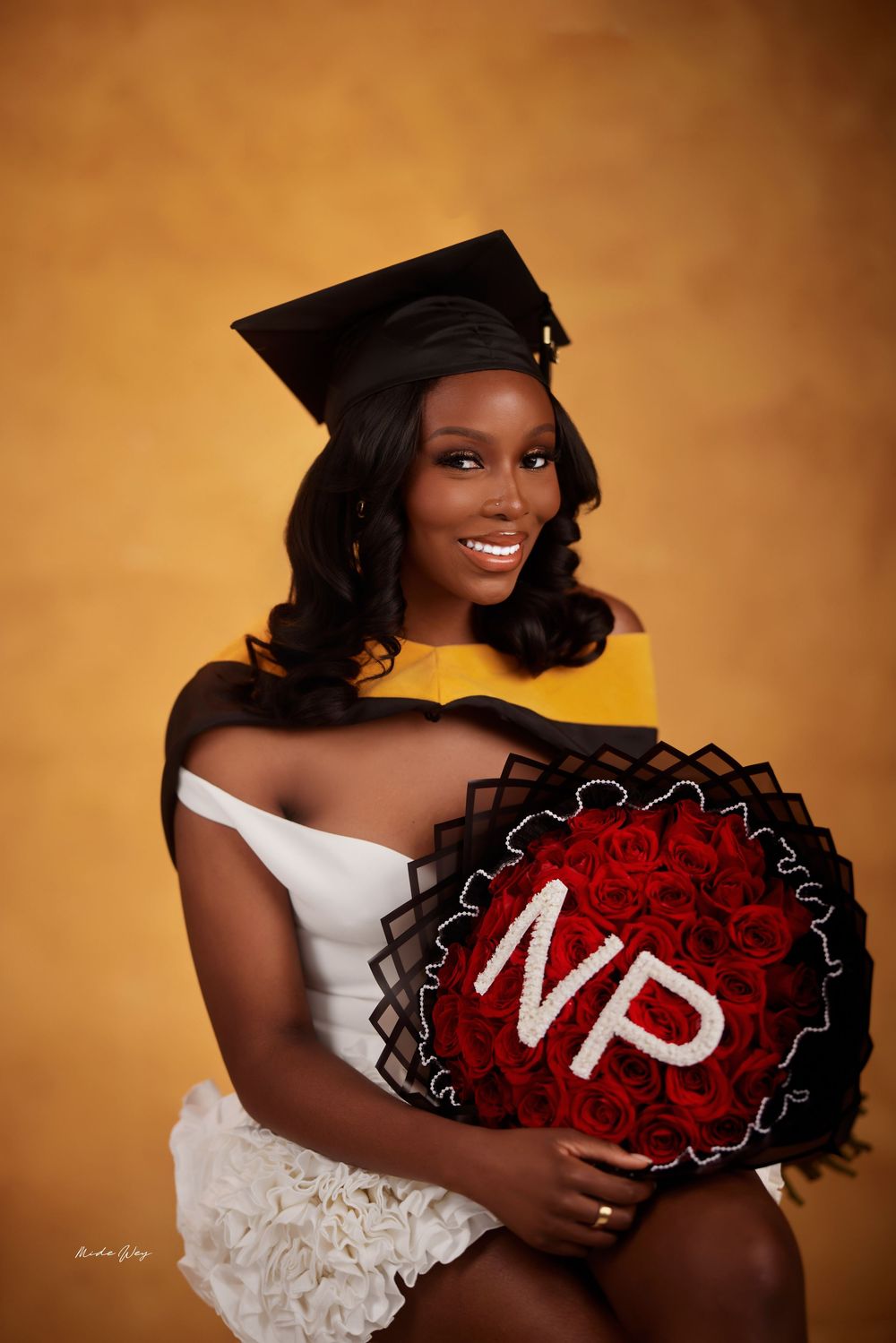 Graduate holding red roses in a white dress against a warm golden background during graduation photo session.