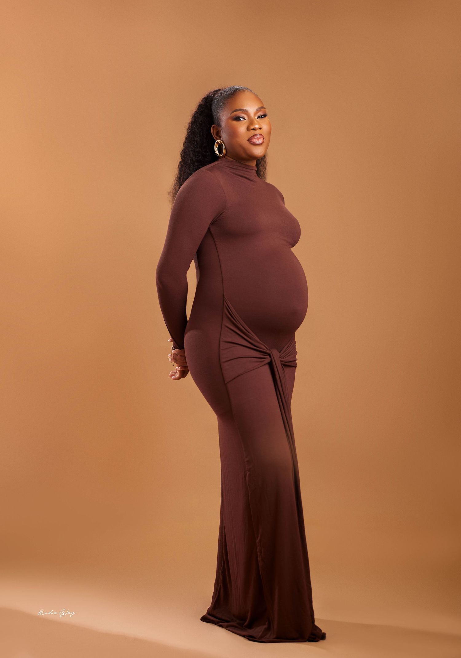 A person wearing a brown turtleneck dress poses in different angles against a beige studio backdrop.