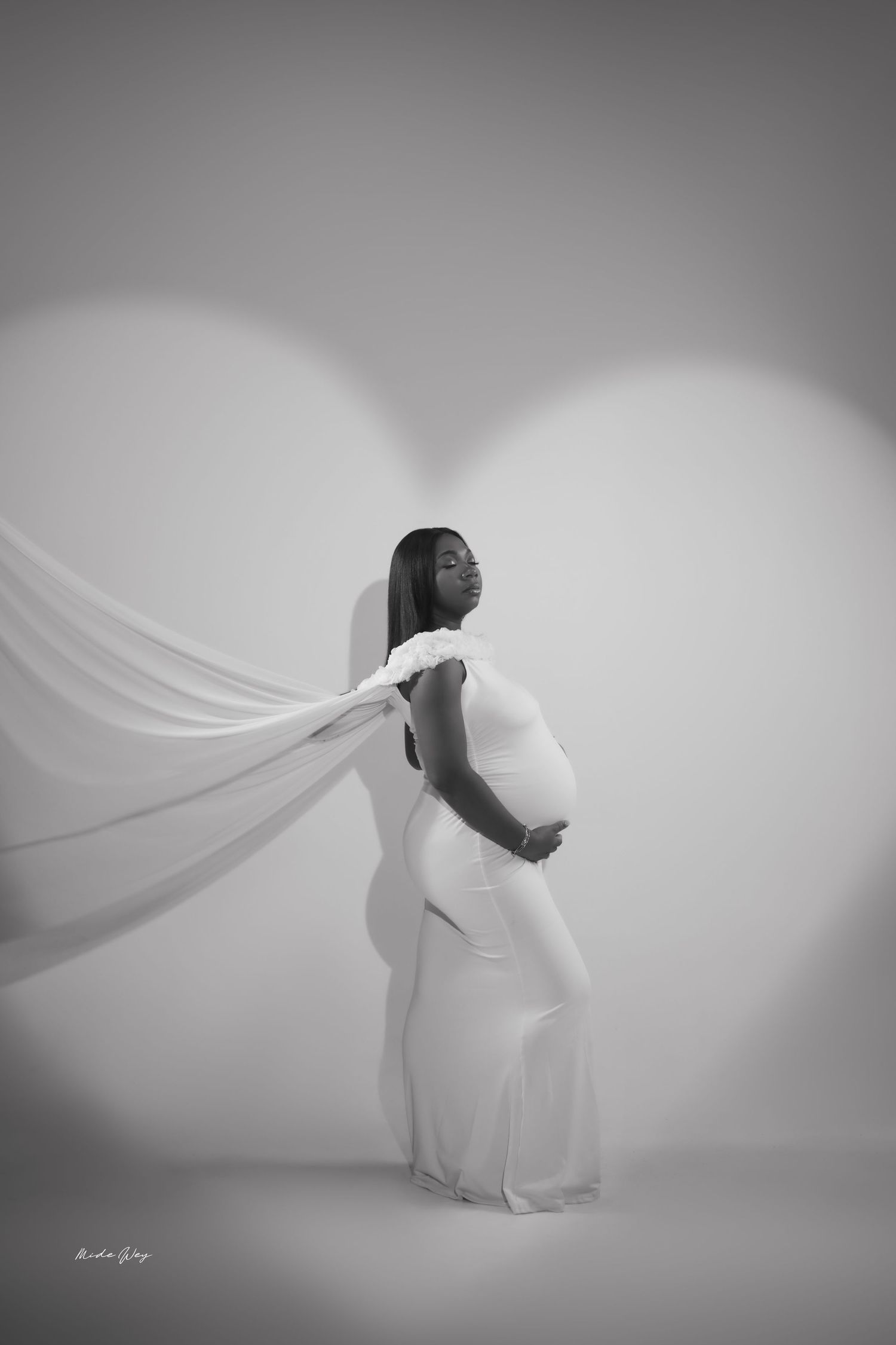 Artistic black and white maternity photo with flowing white fabric against light background.