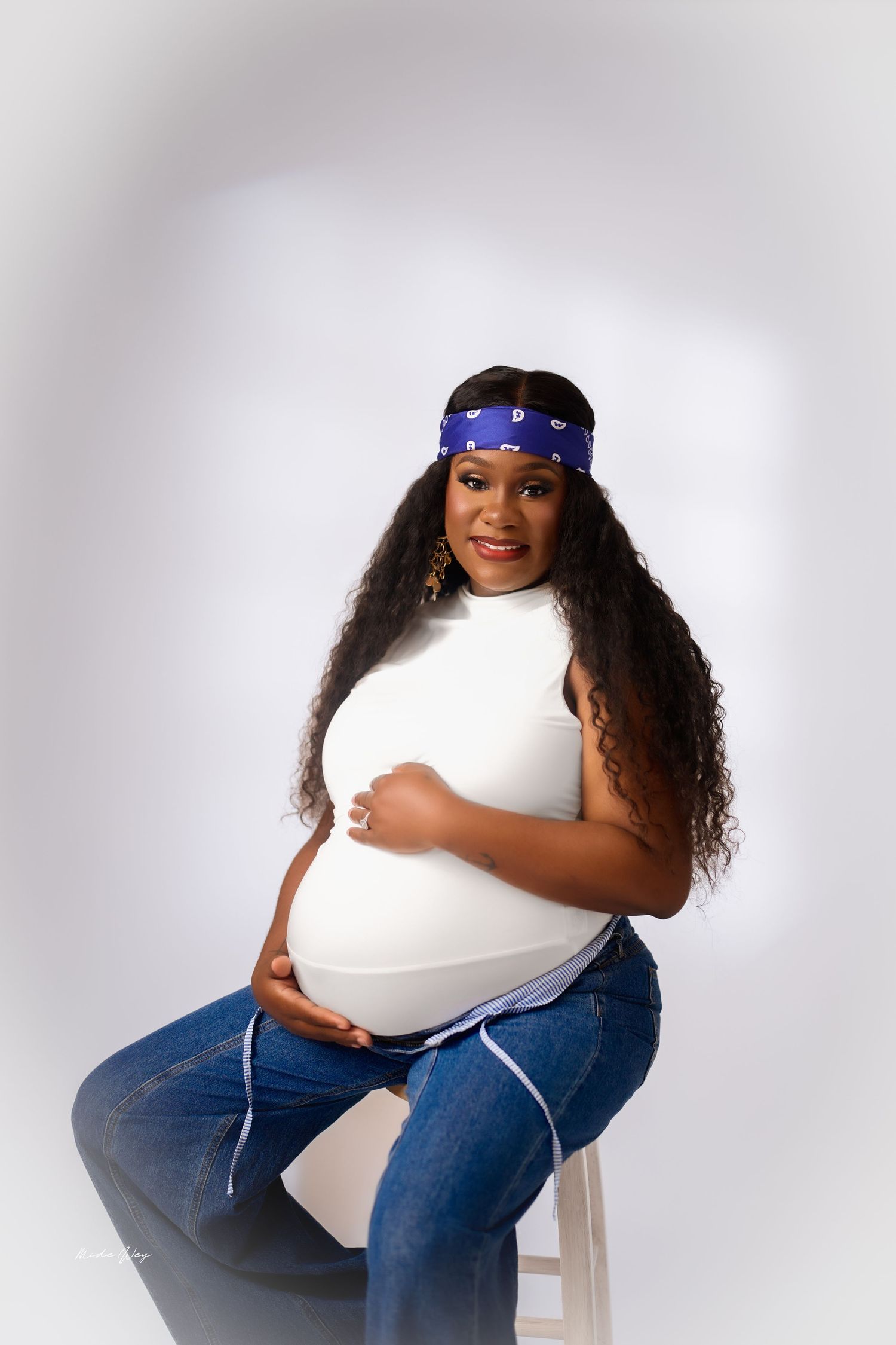 Woman in blue jeans and bandana poses with heart-shaped pillow in studio against white background.