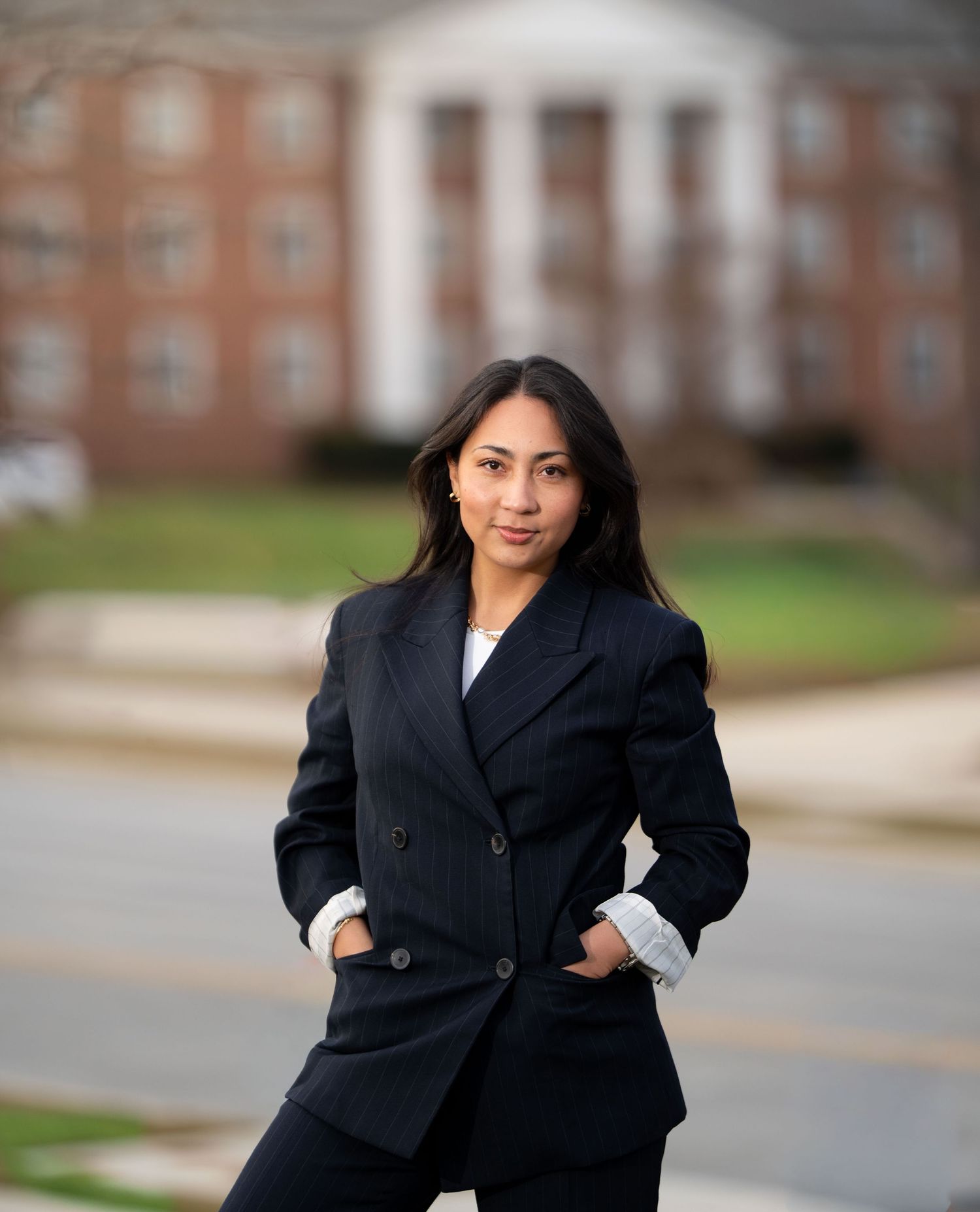 Professional wearing a black blazer poses confidently in front of a brick building with white columns.