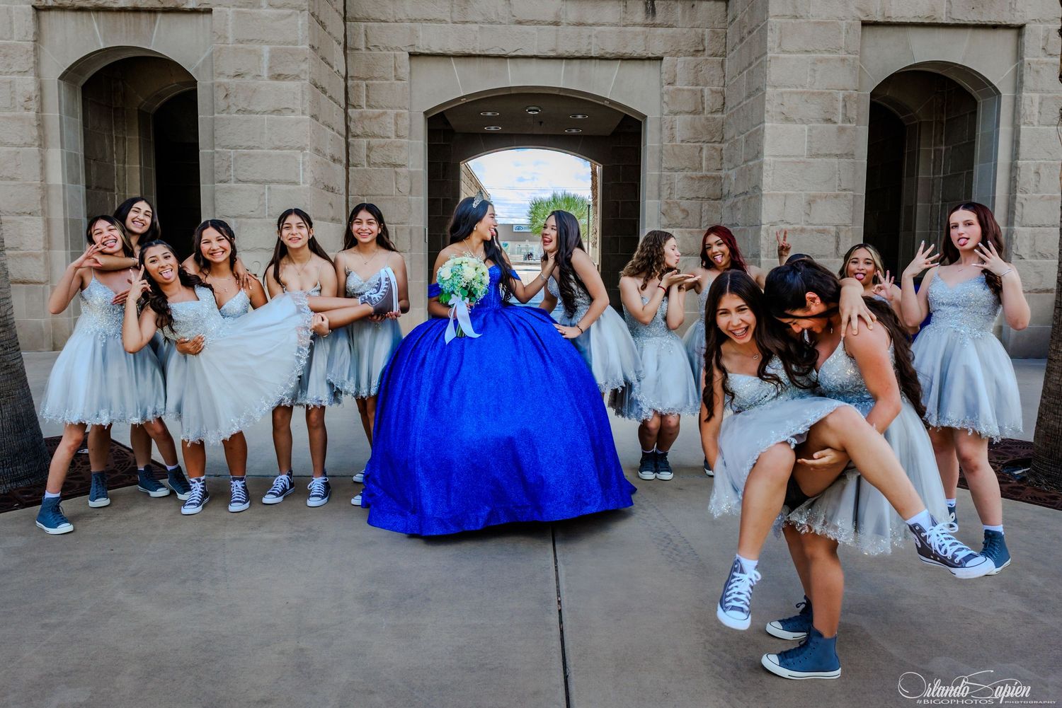 A stunning blue quinceañera dress with floral details photographed in multiple angles against a stone wall backdrop.