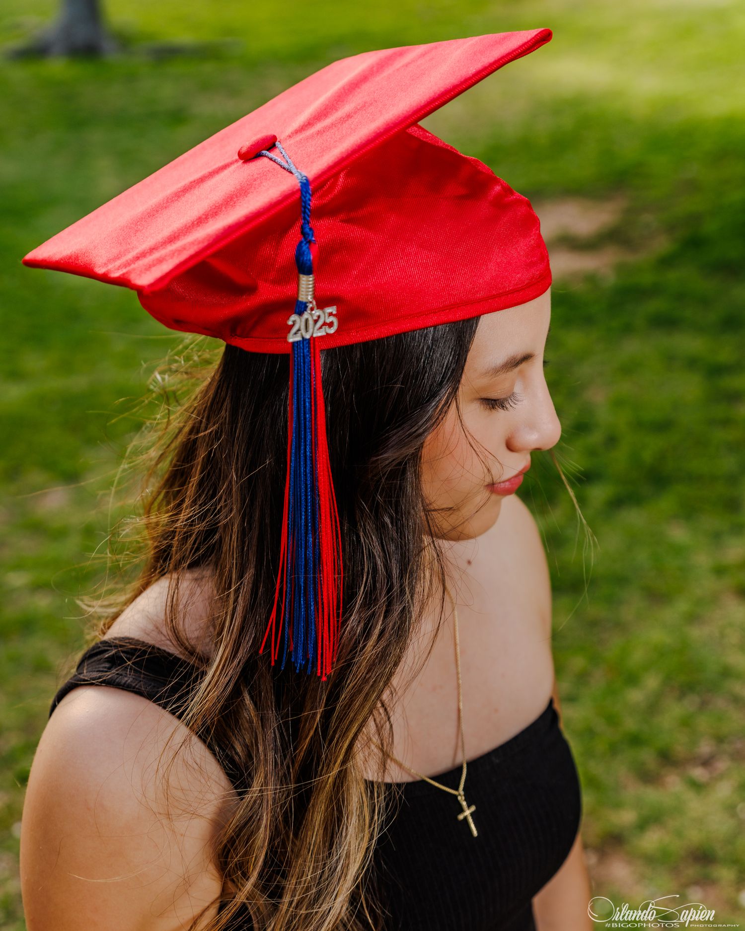 Graduate in red cap with blue tassel poses for artistic graduation photos outdoors.