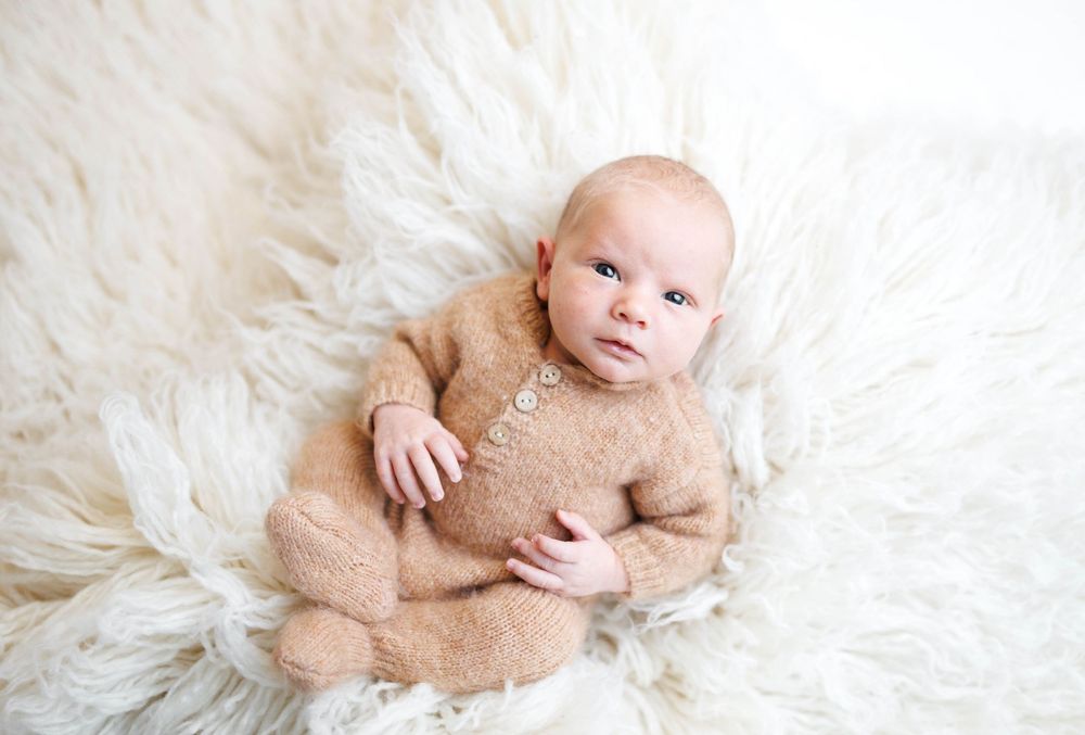 Baby wearing soft beige outfit lying on white fluffy rug during newborn photo session.  lawton oklahoma newborn photographer, lawton ok