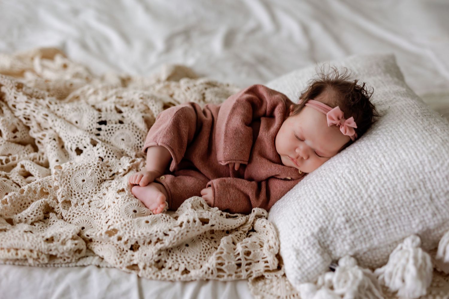 Baby in brown bear costume sits against backdrop with balloons and teddy bears for first birthday photoshoot.