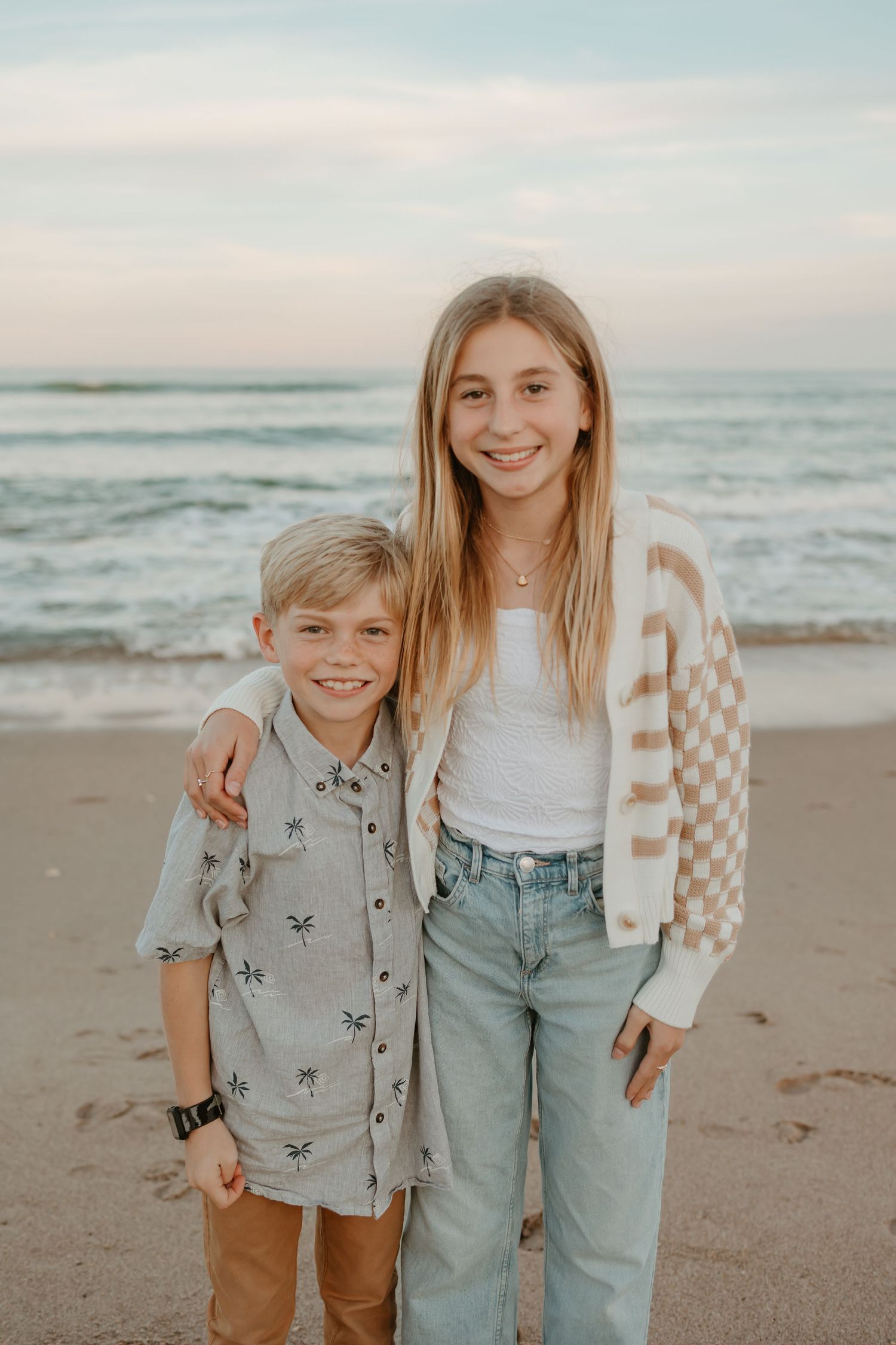 Two children smiling together on beach in casual clothing during family photo shoot.