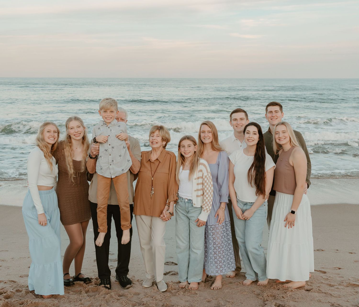 Large family group photo session on the beach wearing coordinated pastel and neutral colors.
