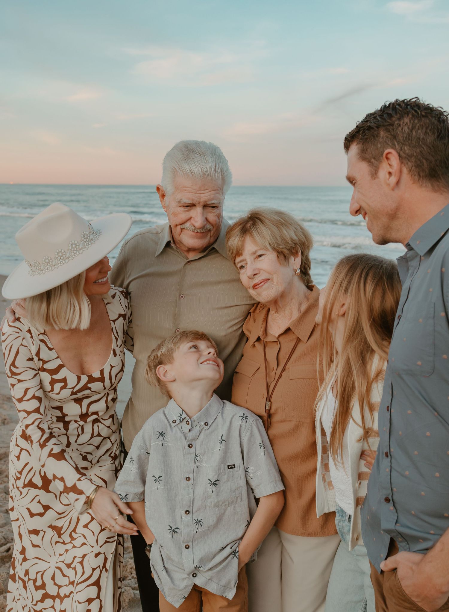 Extended family gathering at sunset on a beach in coordinated neutral outfits.