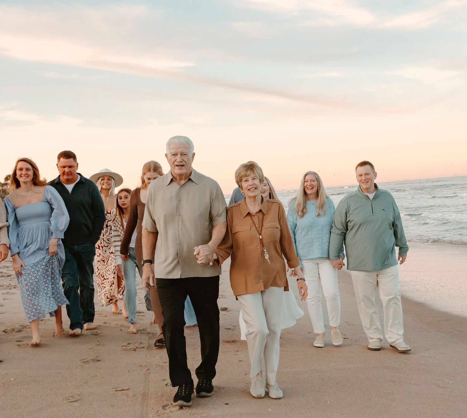 Family group walking together on sandy beach at sunset wearing coordinated neutral colors.