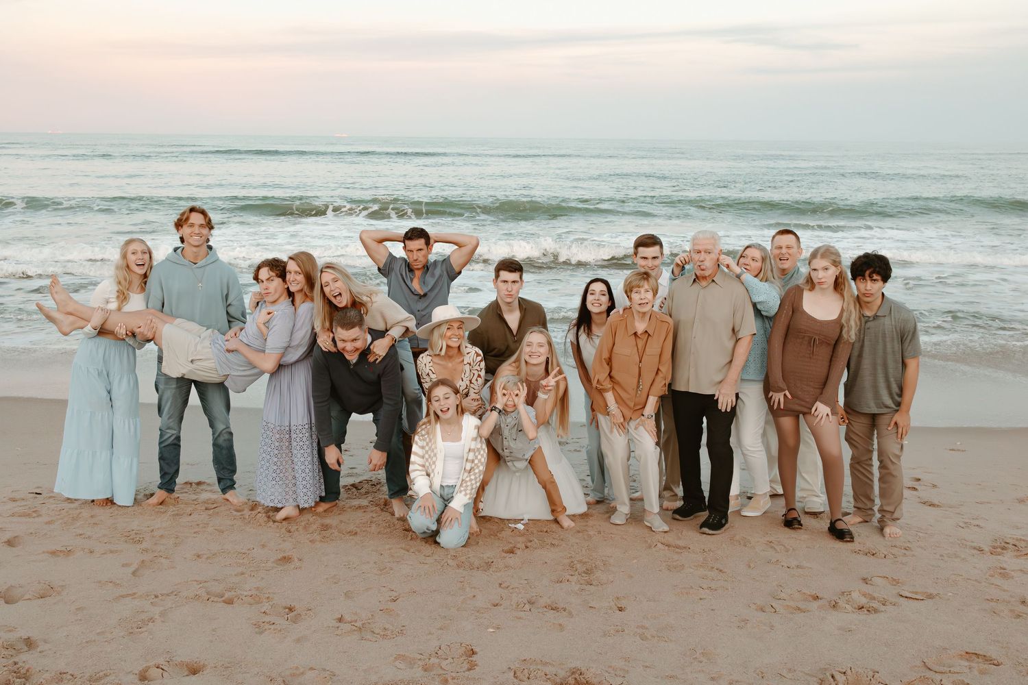Large family group photo session on sandy beach with ocean waves in background at dusk.