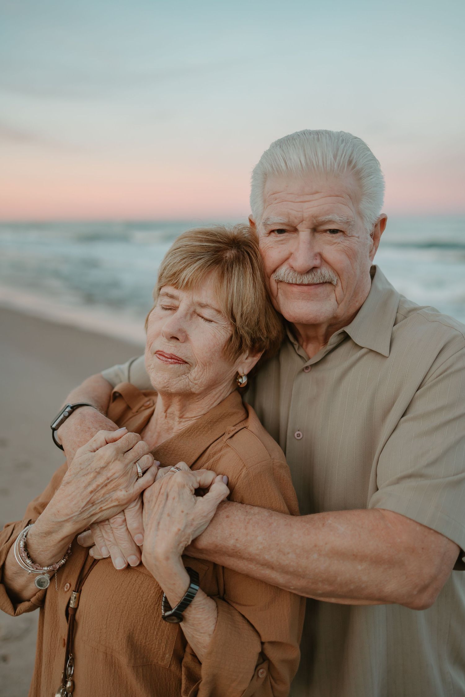 Playful couple embracing and laughing together on beach during golden hour photo session.