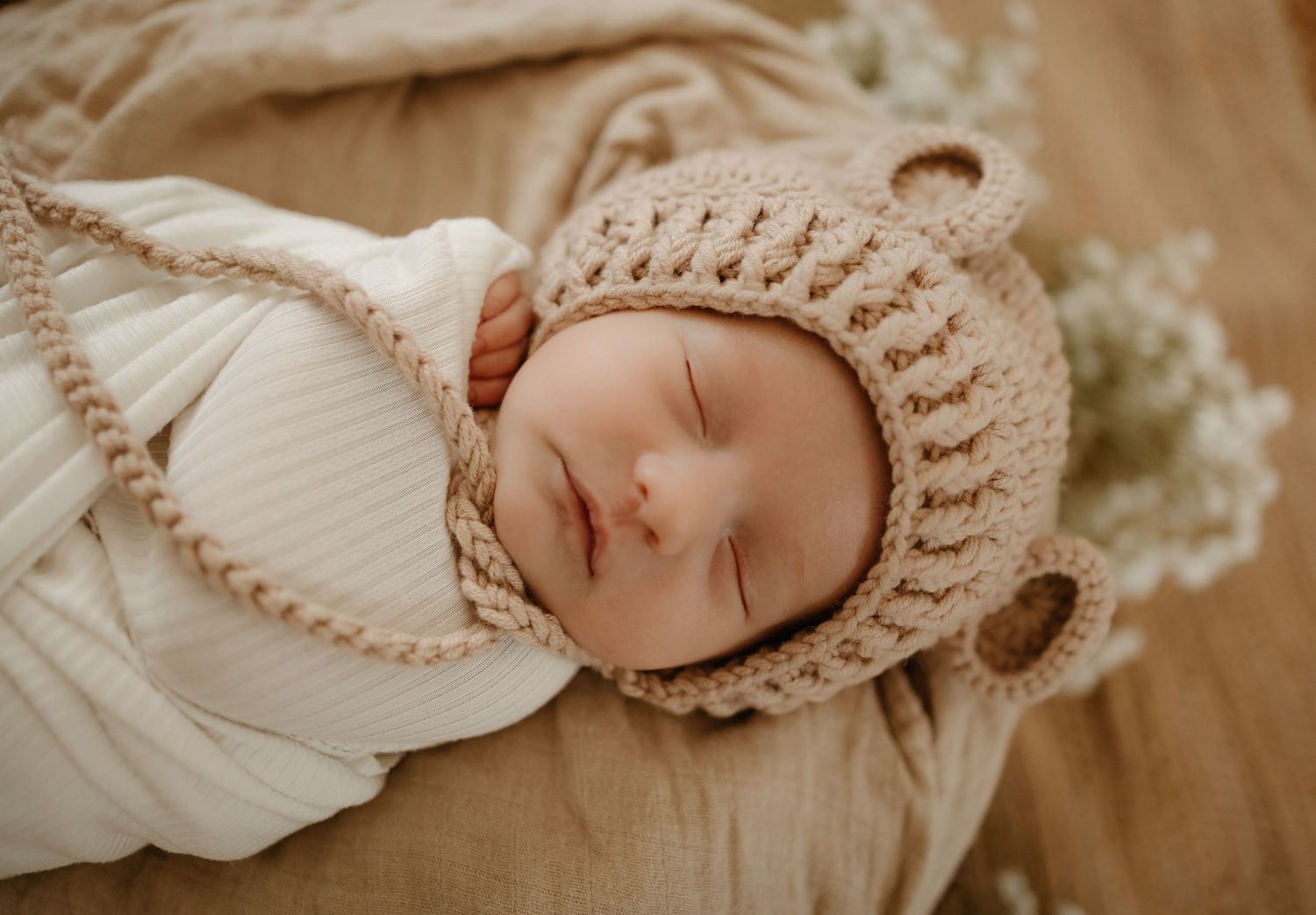 Sleeping newborn wearing a knit bonnet in warm neutral tones.