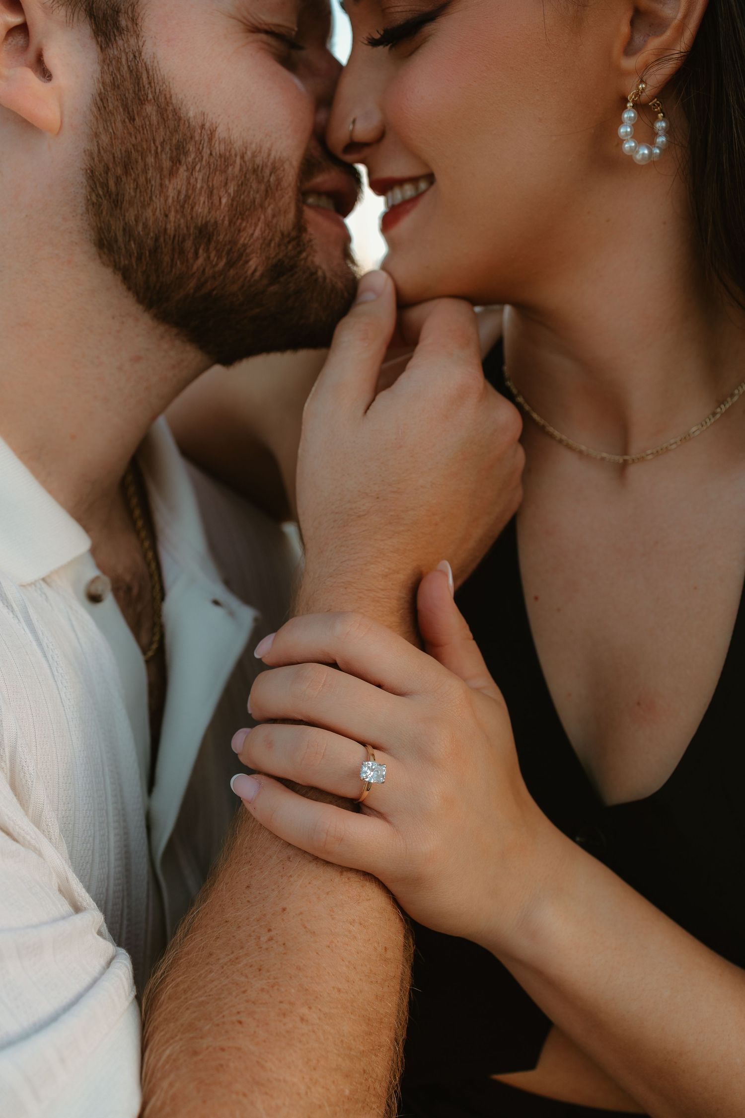 Close up of a romantic couple sharing an intimate kiss with a diamond ring visible.