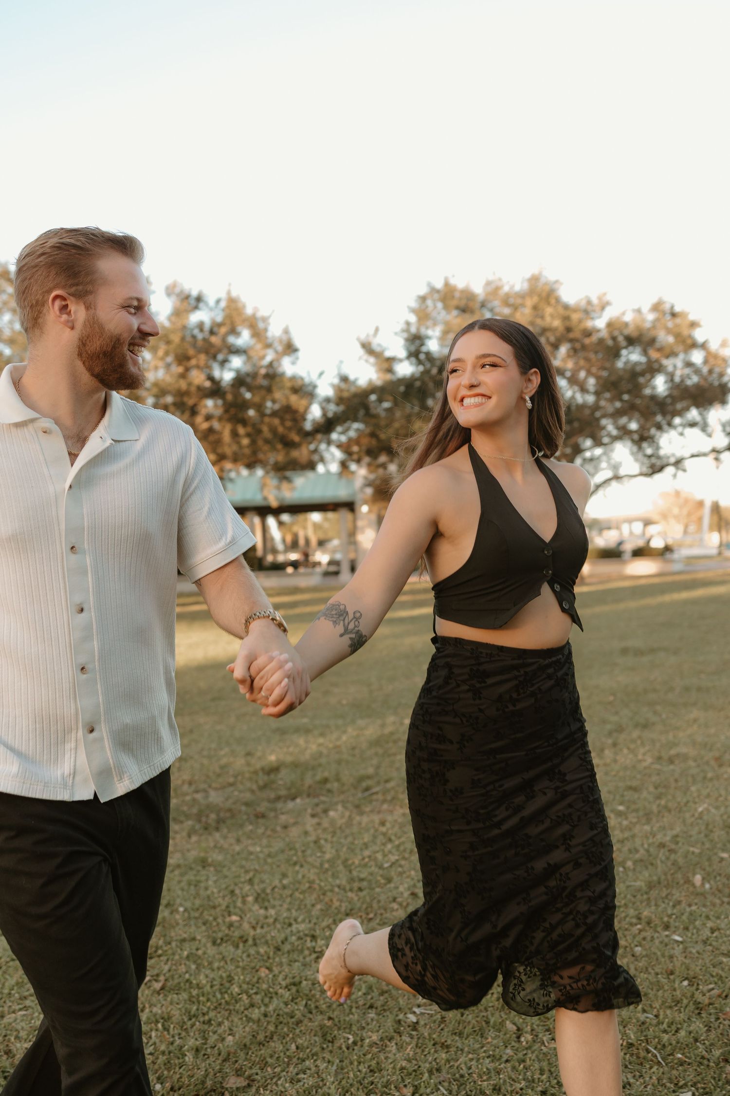 Couple running and laughing together in a grassy field at sunset.